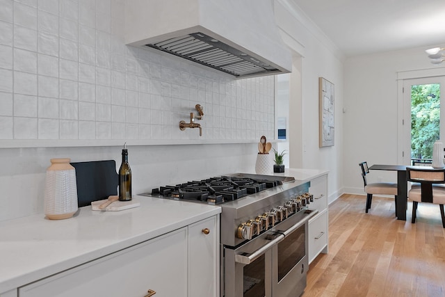 kitchen with crown molding, light hardwood / wood-style flooring, premium range hood, white cabinetry, and range with two ovens