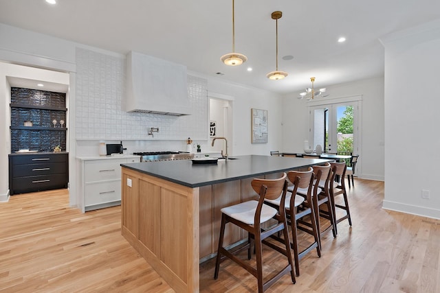 kitchen featuring a kitchen breakfast bar, an island with sink, white cabinets, decorative light fixtures, and custom exhaust hood