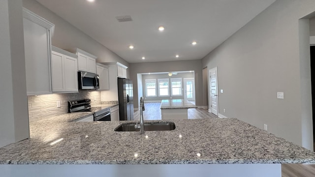 kitchen with stainless steel appliances, sink, light stone counters, and kitchen peninsula