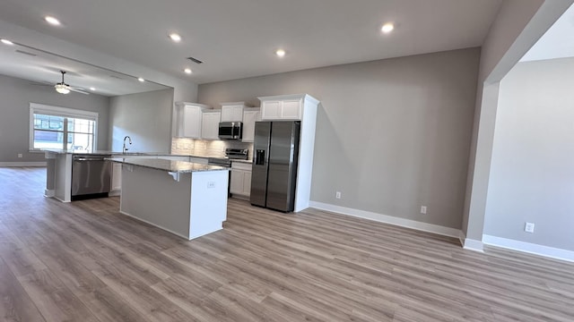 kitchen with appliances with stainless steel finishes, light stone countertops, white cabinets, a kitchen island, and light wood-type flooring