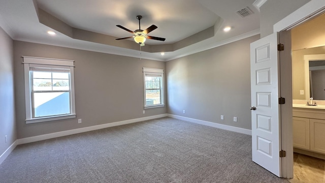 unfurnished bedroom featuring ornamental molding, sink, light carpet, and a tray ceiling