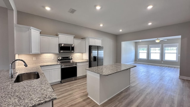 kitchen featuring a kitchen island, white cabinetry, sink, light stone counters, and stainless steel appliances