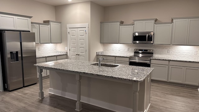 kitchen with tasteful backsplash, appliances with stainless steel finishes, sink, and light stone counters