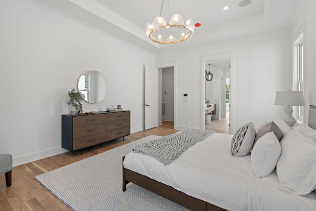 bedroom featuring an inviting chandelier, a tray ceiling, and light hardwood / wood-style flooring