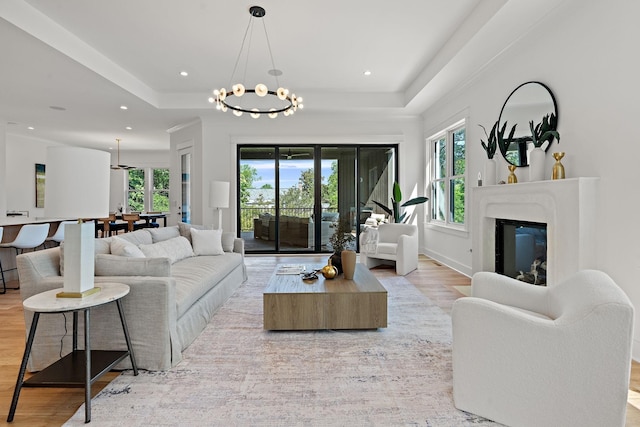 living room with a chandelier, light hardwood / wood-style floors, and a tray ceiling