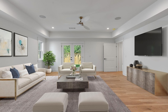 living room with a tray ceiling, light hardwood / wood-style floors, french doors, and ceiling fan