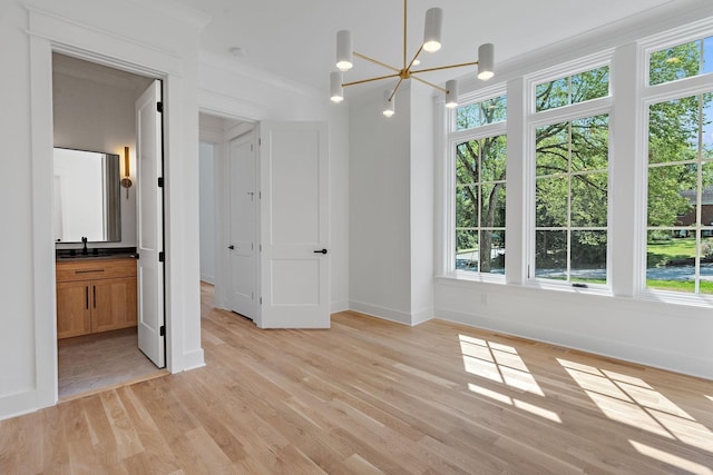 unfurnished bedroom with sink, crown molding, light hardwood / wood-style flooring, ensuite bath, and a notable chandelier