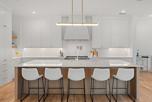 kitchen featuring an island with sink, custom exhaust hood, and white cabinets