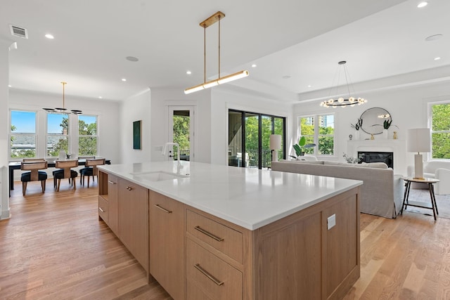 kitchen featuring pendant lighting, sink, a large island, a premium fireplace, and light wood-type flooring