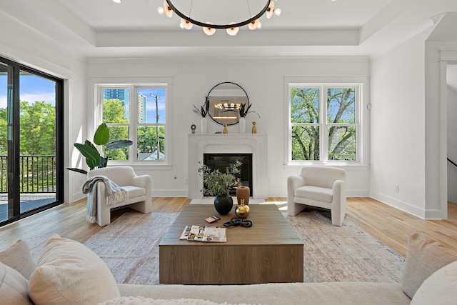 living room featuring a chandelier, a high end fireplace, a raised ceiling, and light hardwood / wood-style floors