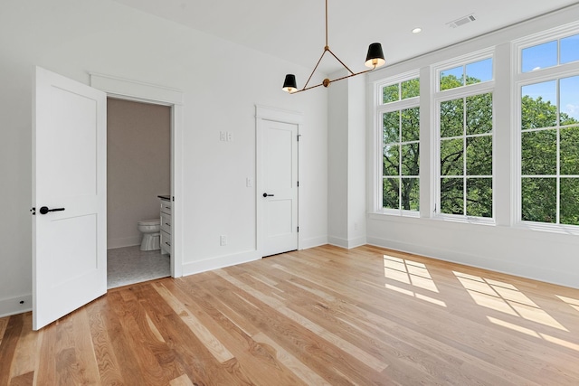 unfurnished bedroom featuring multiple windows, connected bathroom, a chandelier, and light wood-type flooring