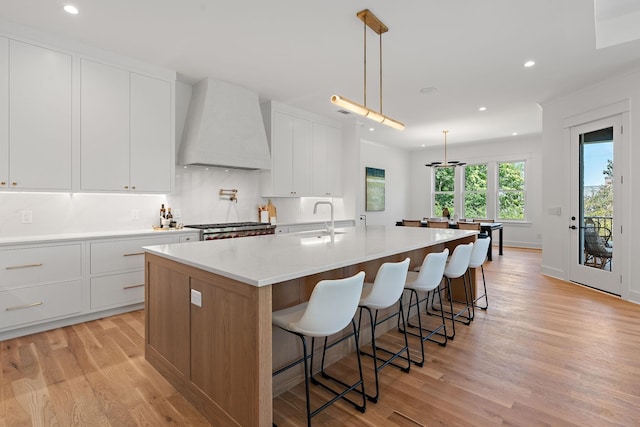 kitchen featuring pendant lighting, white cabinetry, sink, custom exhaust hood, and a large island with sink