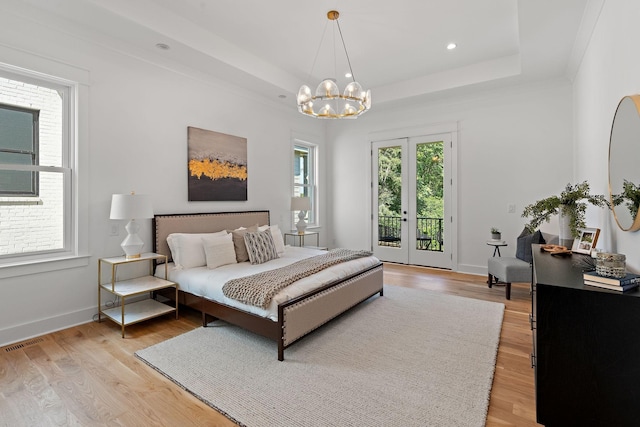 bedroom featuring light hardwood / wood-style flooring, access to outside, a raised ceiling, and an inviting chandelier