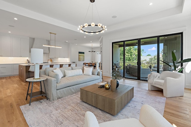 living room with an inviting chandelier, a tray ceiling, and light wood-type flooring