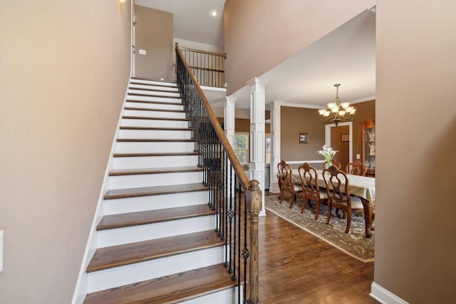 stairs featuring crown molding, hardwood / wood-style floors, decorative columns, a high ceiling, and a chandelier