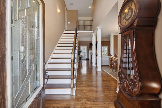 foyer with dark wood-type flooring, a towering ceiling, and ornate columns