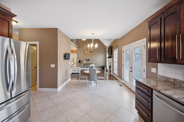 kitchen with light tile patterned flooring, an inviting chandelier, vaulted ceiling, dark stone countertops, and appliances with stainless steel finishes