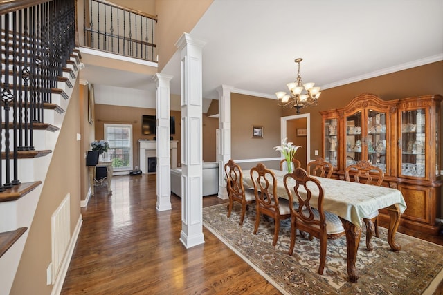 dining room with an inviting chandelier, a towering ceiling, ornamental molding, dark hardwood / wood-style flooring, and ornate columns