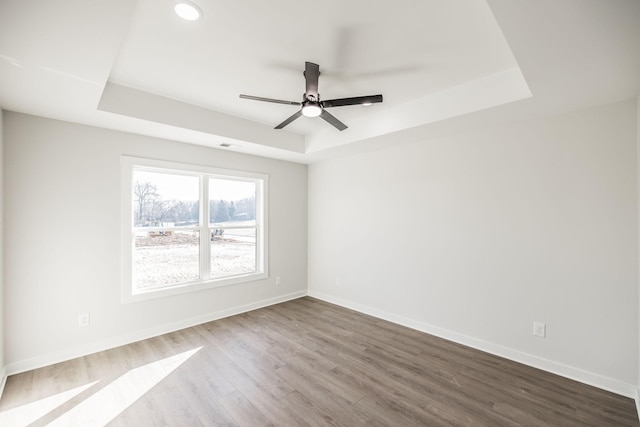 spare room with wood-type flooring, ceiling fan, and a tray ceiling