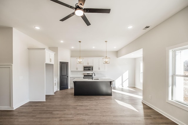 kitchen featuring sink, white cabinetry, wood-type flooring, decorative light fixtures, and an island with sink