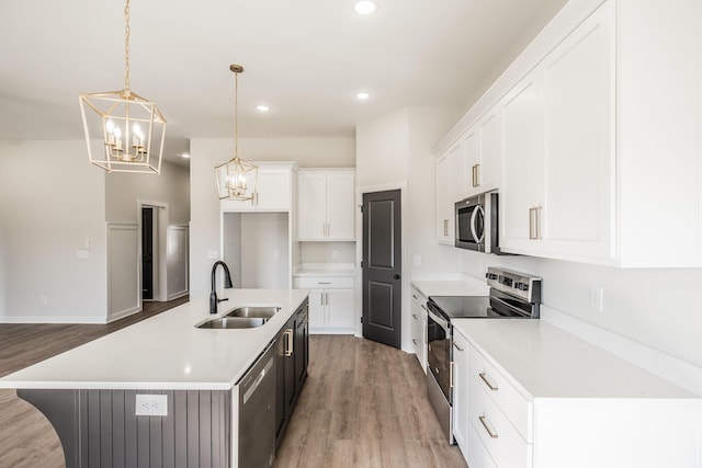 kitchen featuring sink, white cabinetry, stainless steel appliances, an island with sink, and decorative light fixtures