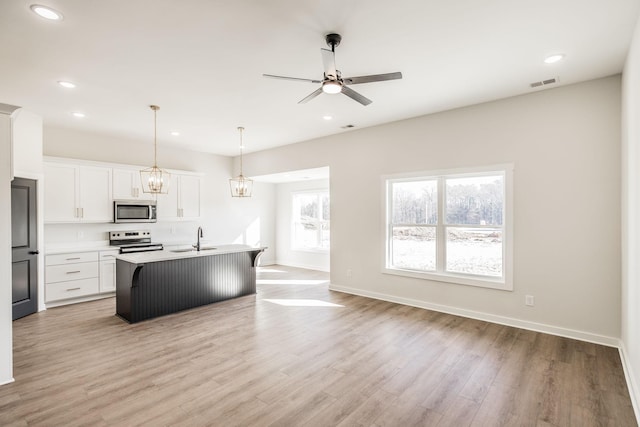 kitchen with appliances with stainless steel finishes, pendant lighting, white cabinetry, sink, and a kitchen island with sink