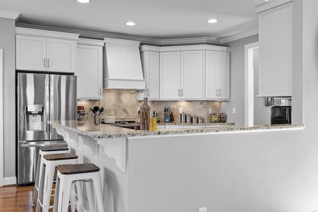 kitchen featuring white cabinetry, stainless steel fridge, ornamental molding, light stone countertops, and custom range hood