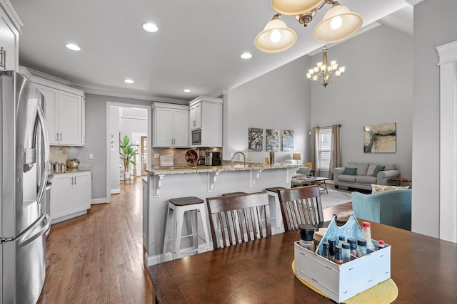 dining space with high vaulted ceiling, sink, a chandelier, ornamental molding, and light hardwood / wood-style floors