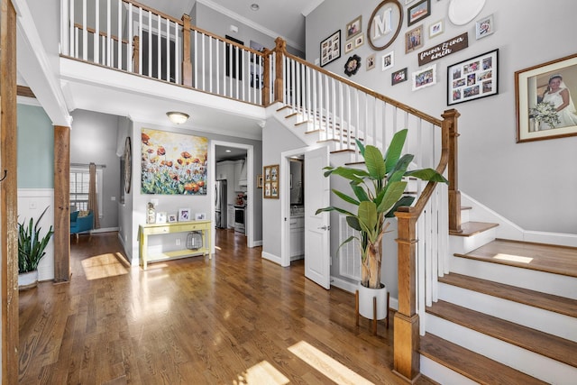 staircase featuring wood-type flooring, a towering ceiling, and ornamental molding