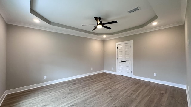 unfurnished room with wood-type flooring, ornamental molding, ceiling fan, and a tray ceiling