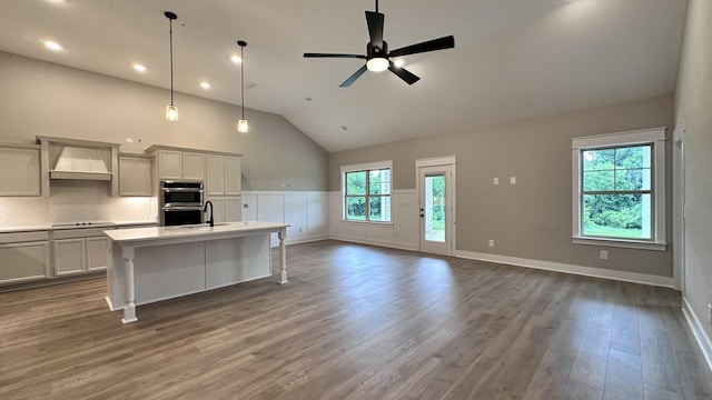 kitchen featuring double oven, a kitchen breakfast bar, custom range hood, an island with sink, and decorative light fixtures