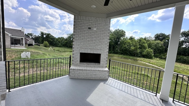 view of patio with an outdoor brick fireplace, a water view, and ceiling fan