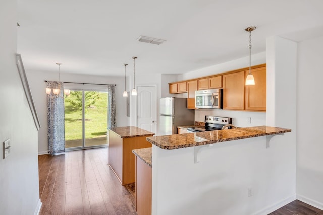 kitchen with pendant lighting, stone countertops, appliances with stainless steel finishes, a kitchen bar, and kitchen peninsula