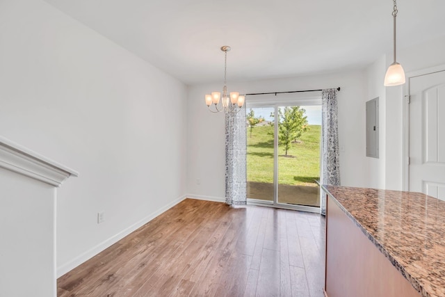 unfurnished dining area featuring hardwood / wood-style flooring, electric panel, and a chandelier