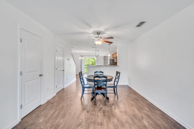 dining area featuring ceiling fan with notable chandelier and wood-type flooring