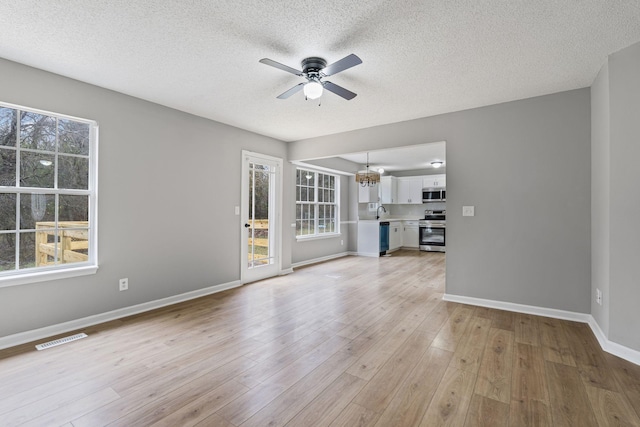 unfurnished living room with a textured ceiling, ceiling fan with notable chandelier, sink, and light hardwood / wood-style flooring