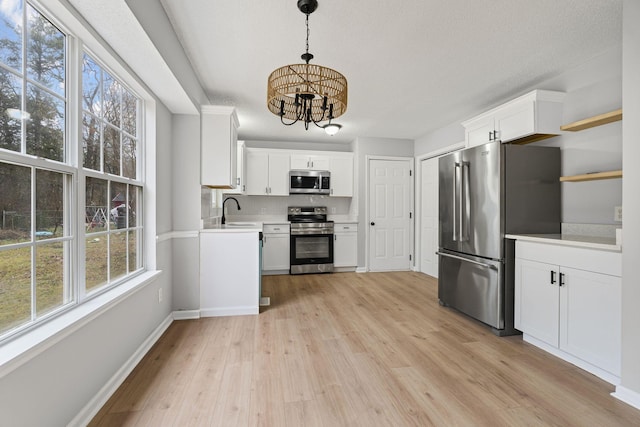 kitchen with appliances with stainless steel finishes, white cabinets, light hardwood / wood-style floors, and pendant lighting