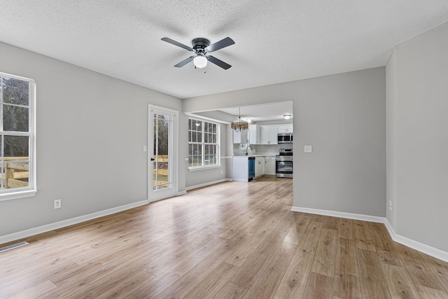 unfurnished living room with a textured ceiling, ceiling fan with notable chandelier, and light hardwood / wood-style flooring