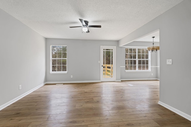 spare room with a textured ceiling, hardwood / wood-style floors, and ceiling fan with notable chandelier