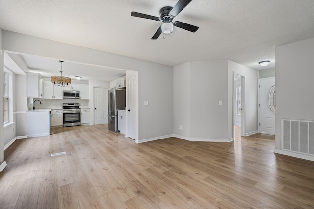 unfurnished living room with ceiling fan with notable chandelier, sink, light hardwood / wood-style floors, and a textured ceiling