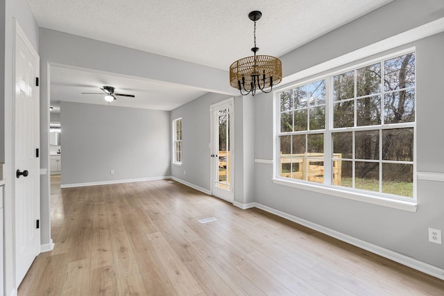 unfurnished dining area with a textured ceiling, a wealth of natural light, and light hardwood / wood-style flooring