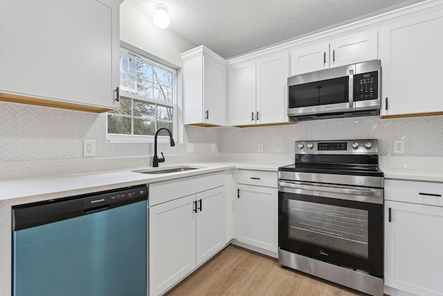 kitchen with sink, appliances with stainless steel finishes, white cabinets, and light hardwood / wood-style flooring