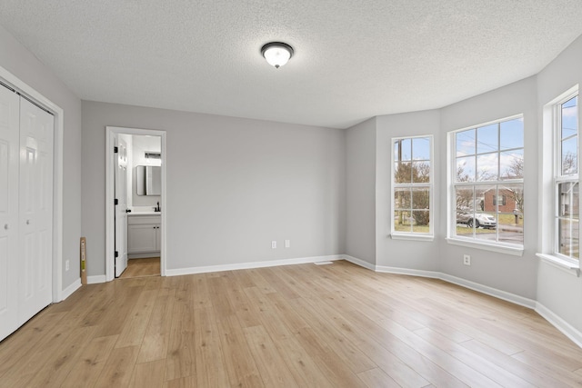 unfurnished bedroom with light wood-type flooring, multiple windows, and a textured ceiling