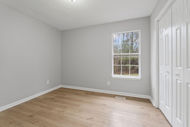 unfurnished bedroom with light wood-type flooring, a textured ceiling, and a closet