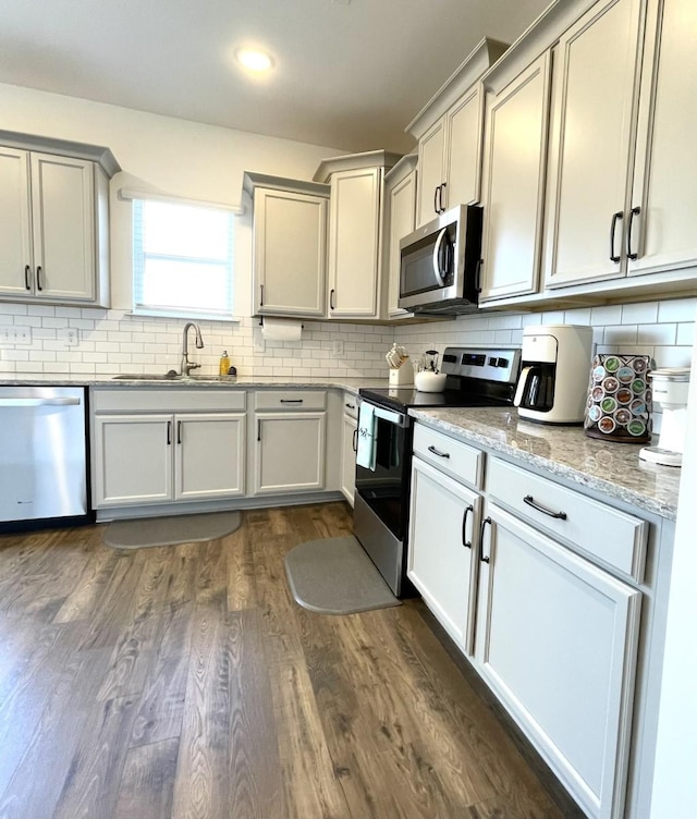 kitchen featuring appliances with stainless steel finishes, sink, backsplash, light stone counters, and dark wood-type flooring