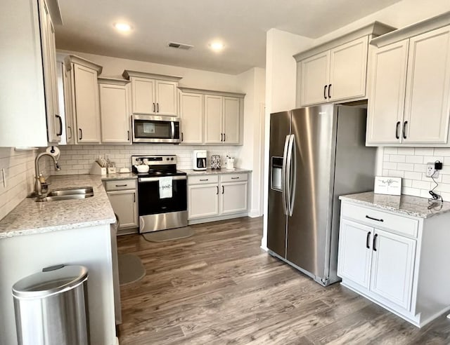 kitchen with sink, hardwood / wood-style flooring, appliances with stainless steel finishes, light stone counters, and decorative backsplash