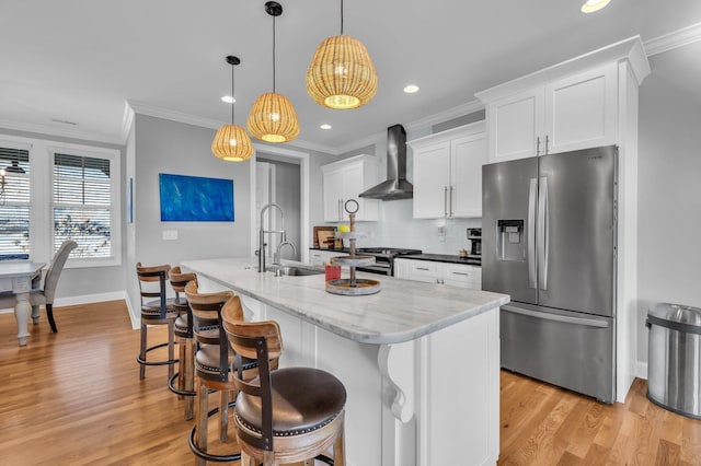 kitchen featuring pendant lighting, white cabinetry, a kitchen island with sink, stainless steel appliances, and wall chimney range hood