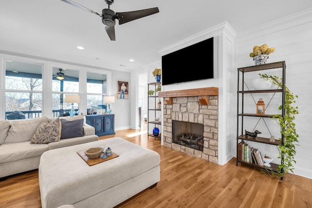 living room featuring a stone fireplace, ornamental molding, light hardwood / wood-style floors, and ceiling fan