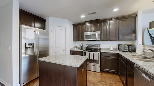 kitchen featuring appliances with stainless steel finishes, sink, dark brown cabinets, a center island, and dark wood-type flooring