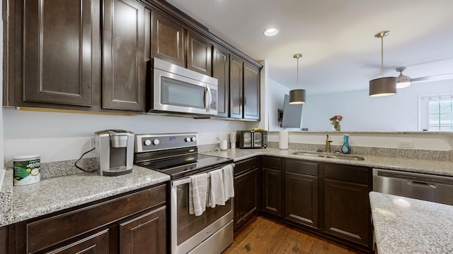 kitchen featuring appliances with stainless steel finishes, sink, hanging light fixtures, light stone counters, and dark wood-type flooring